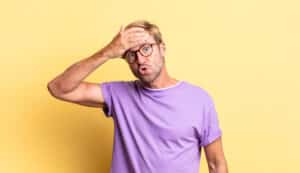hombre con camiseta púrpura, sosteniendo la frente expresión estresada