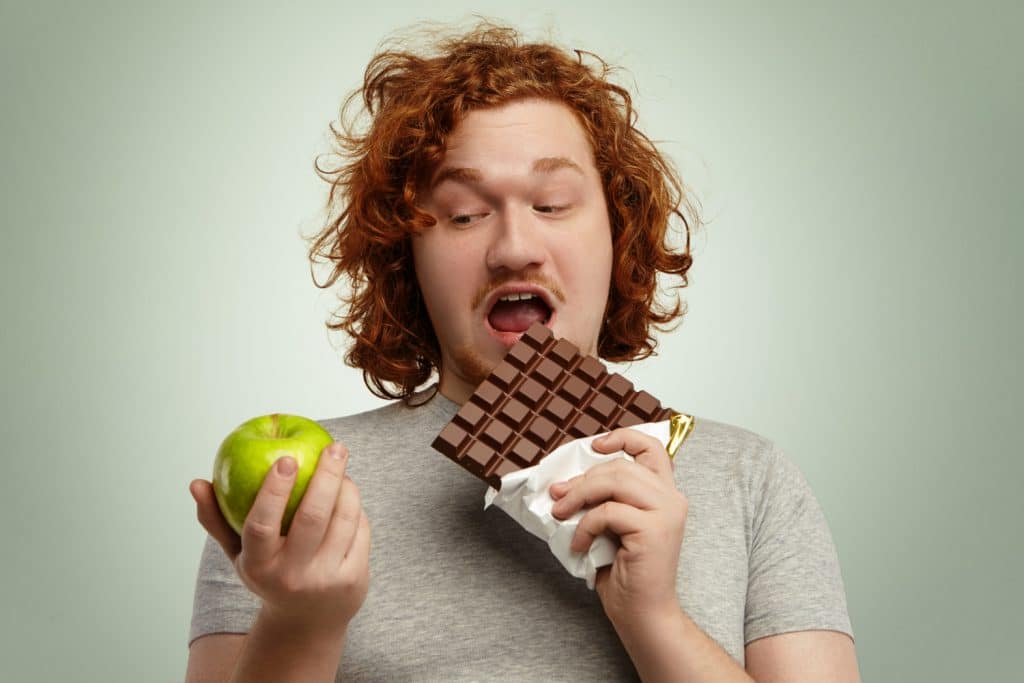 Un hombre muerde una barra de chocolate, pero mira una manzana verde de forma equivocada